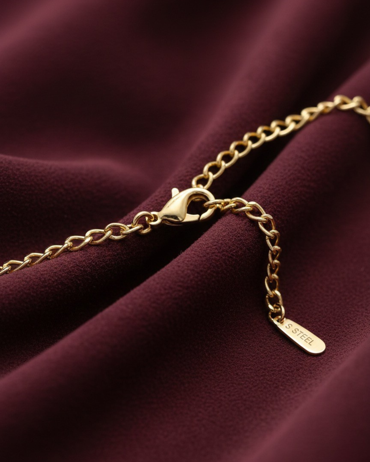 Gold chain bracelet on a burgundy fabric background