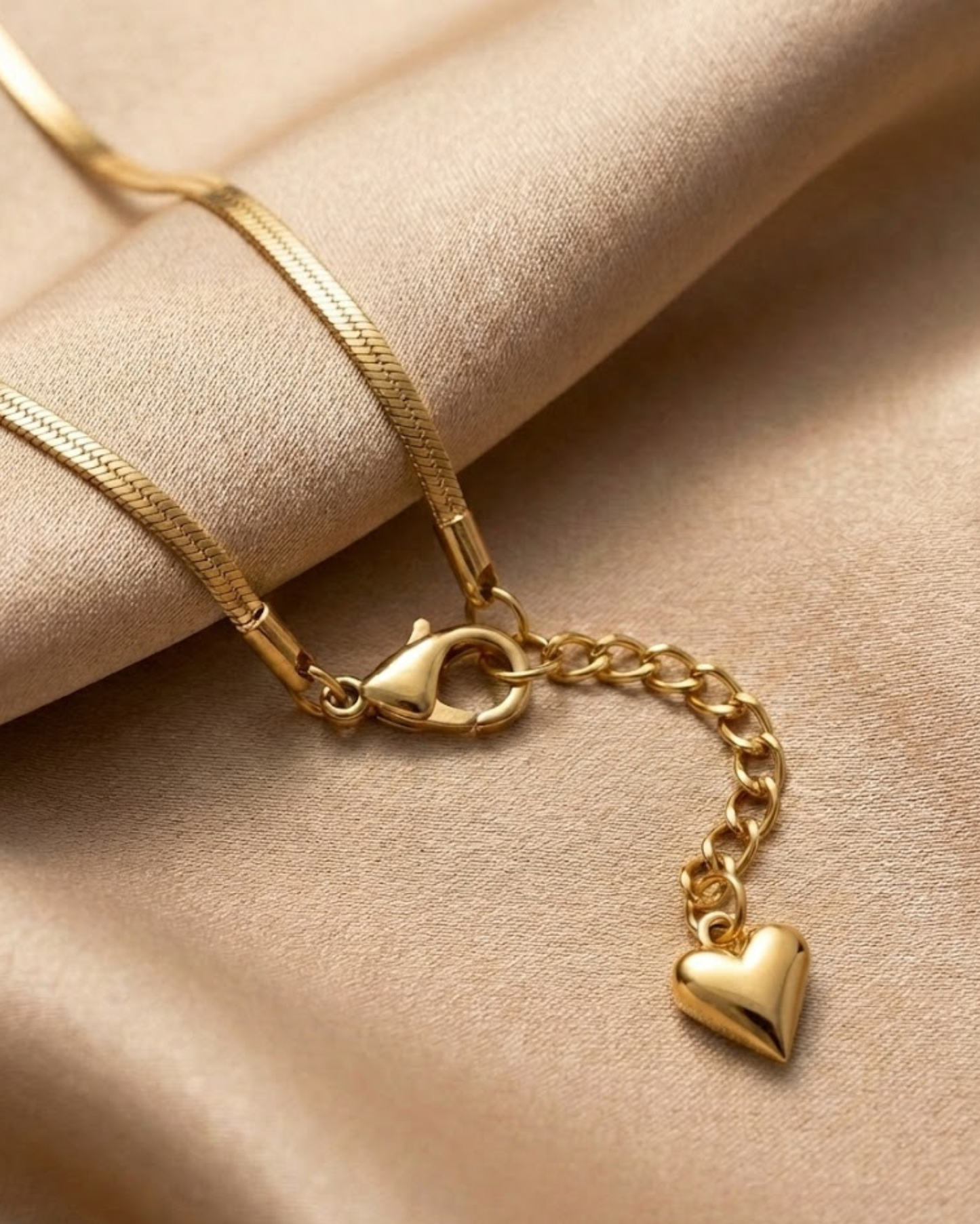 Gold bracelet with a heart charm on a beige fabric background