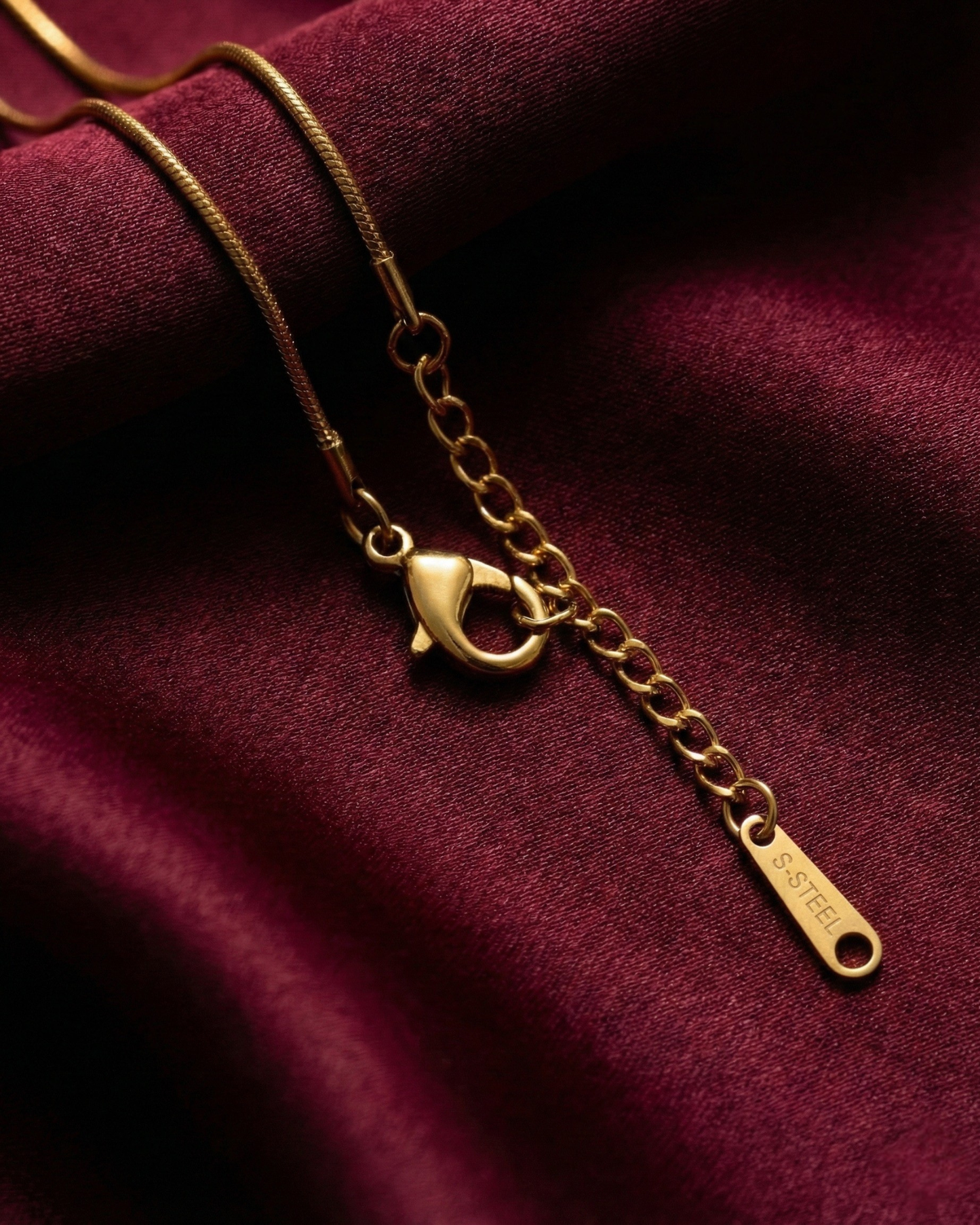 Gold necklace with a pendant on a maroon fabric background