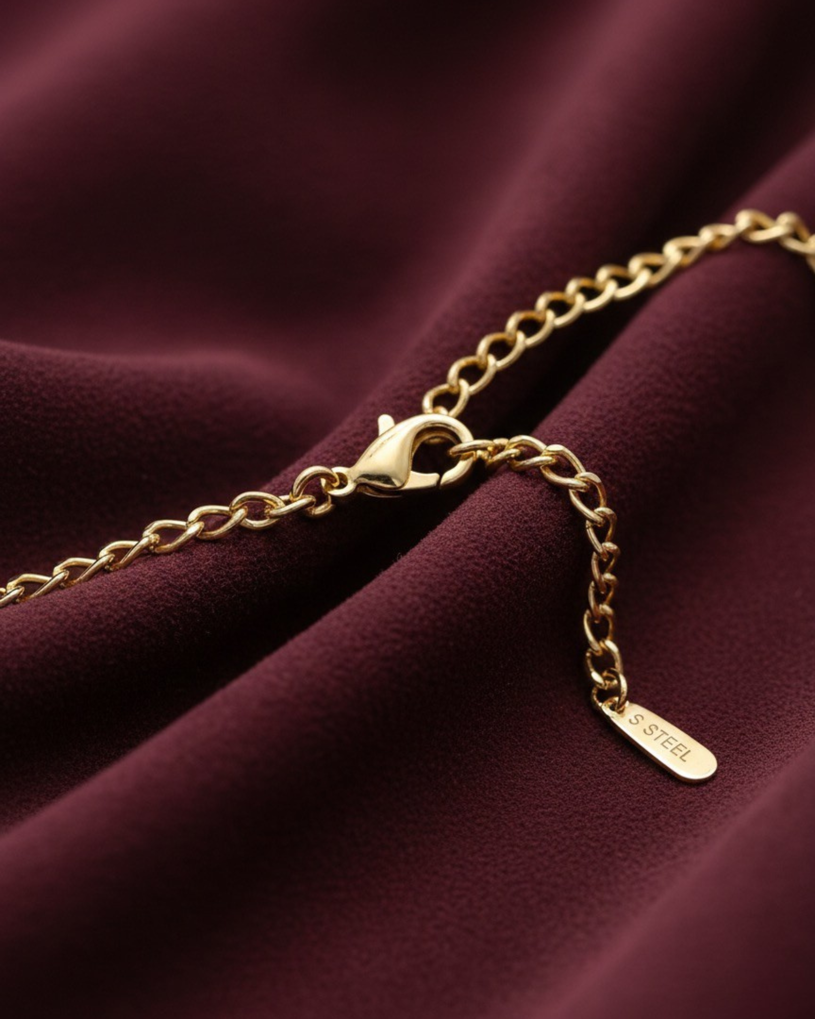 Gold chain bracelet on a burgundy fabric background