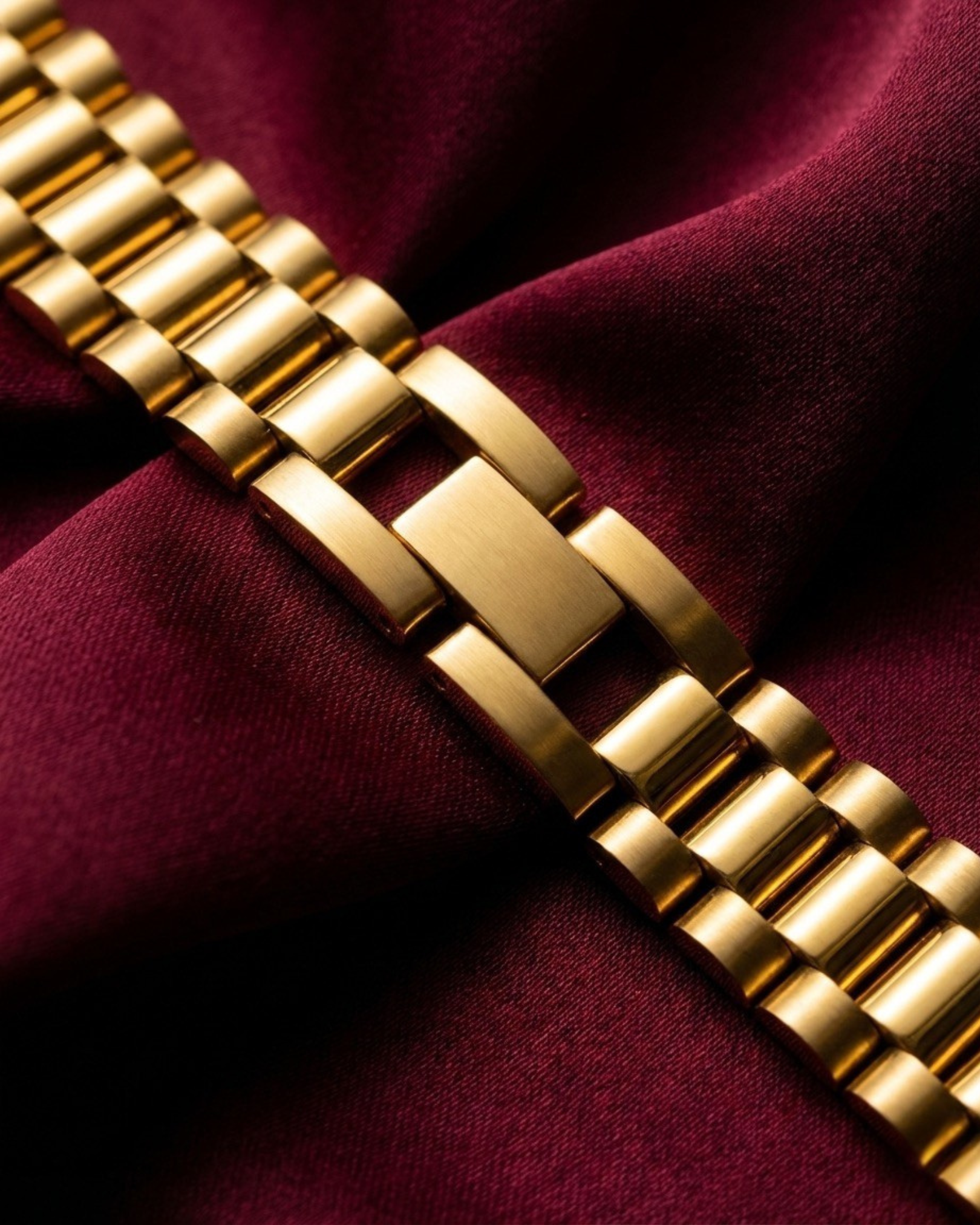 Gold watch bracelet on a burgundy fabric background